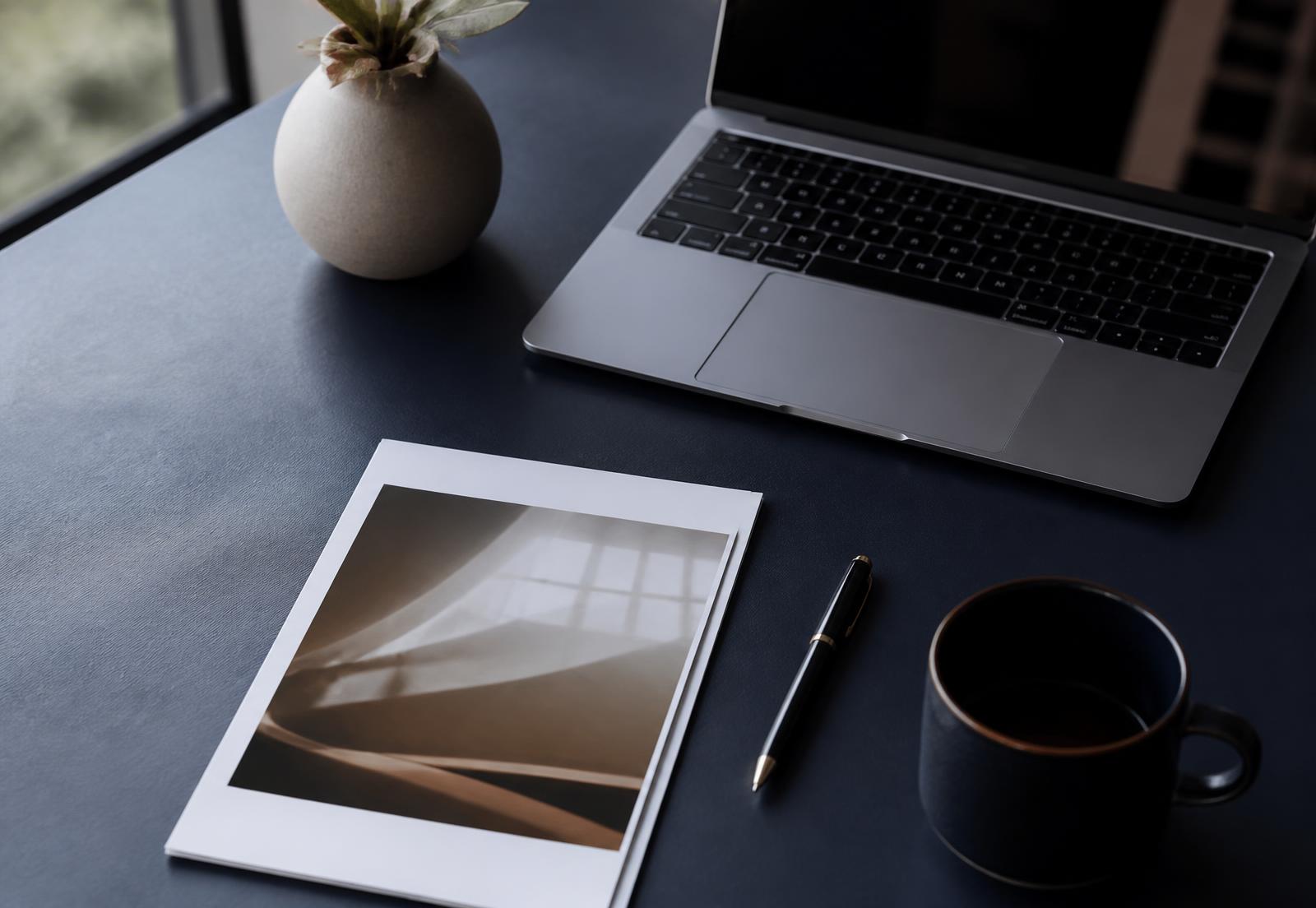 A laptop, a printed document, and a pen arranged on a desk in soft daylight.